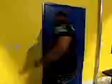 A large man humorously struggles to fit through a small blue door in a yellow room. His expression is amused, emphasizing the playful, comedic tone.
