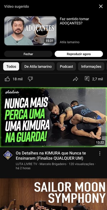 A imagem mostra uma tela de um aplicativo de vídeo sugerindo dois vídeos. O vídeo sugerido no topo tem um título "Faz sentido tomar ADOÇANTES?" e dura 15:31 minutos, apresentado por Atila Lamarino. A imagem do vídeo sugere um homem com uma xícara de café e um frasco de adoçante. Abaixo, há uma seção de filtros com opções "Todos", "De Atila lamarino", "Podcast" e "Informações". O vídeo sugerido abaixo tem um título "NUNCA MAIS PERCA UMA KIMURA NA GUARDA!" e dura 13:22 minutos, apresentado por LU…