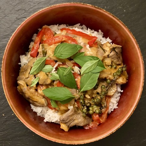 Bowl of rice with Pad Ped on top, which is a kind of red curry with duck breast, red bell pepper and fresh green pepper