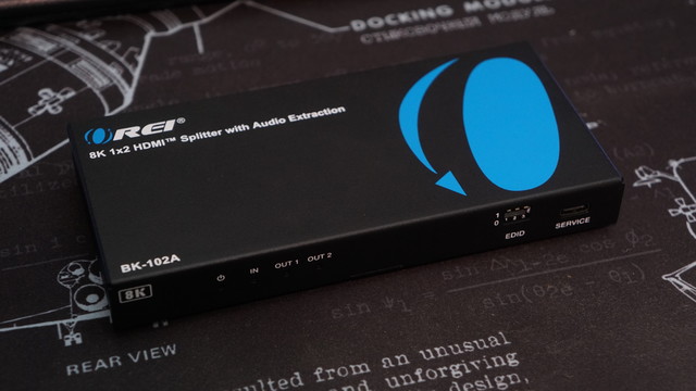The front of the Orei 8K 1x2 HDMI Splitter (BK0102A) showing four LEDs (Power, Input, Output 1, Output 2), an EDID settings set of dip switches, and a USB-C service port.