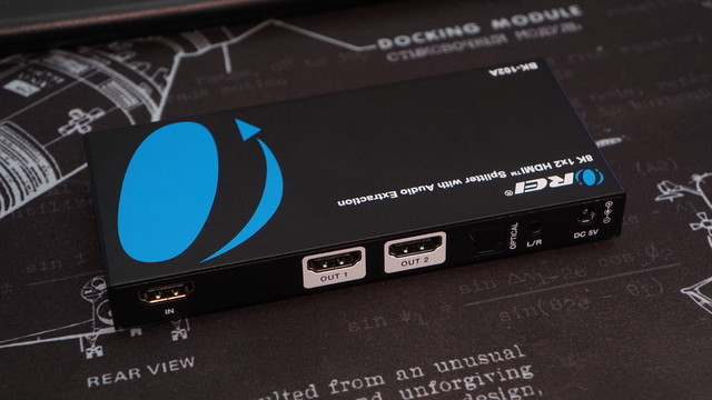 The back of the Orei 8K 1x2 HDMI Splitter (BK0102A) showing the HDMI input and two outputs, an analog headphone output jack, a TOSLINK output, and the 5VDC barrel jack.