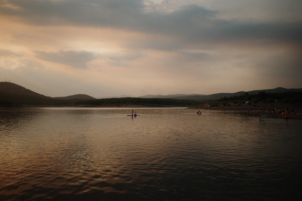 A view of a reservoir in León, Spain, at sunset. The warmer skies are due to the fires in the region. One can see a couple in a stand up paddle.