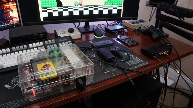 A picture of an NES in a clear acrylic shell connected to a RetroTINK 5X on top of a desk.