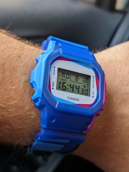 Casio G-Shock wristwatch. Band is blue, bezel is blue with hints of light blue and magenta, dial is white. Digital display.