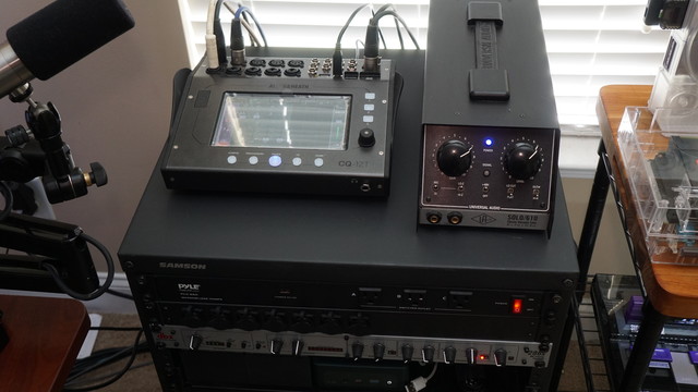 A picture of the Earthworks Audio Ethos microphone on a microphone arm, the top of an audio rack showing an Allen&Heath CQ-12T mixer beside a Universal Audio SOLO/610.  Below those is a dbx 286s audio processor strip (1U).