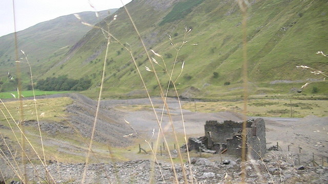derelict mine building in a deep valley, a few stems of grass in foreground
