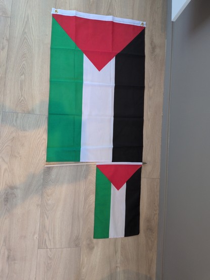 Two Palestinian flags laying on a light wooden floor The flags feature horizontal stripes of black, white, and green with a red triangle on the left.