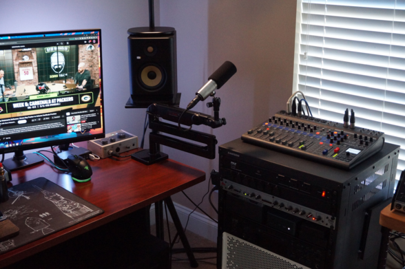 A picture of the current RKR G5 speaker sitting on a speaker stand next to a microphone and a monitor.