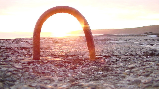 sunrise through a vertical staple on a harbour wall