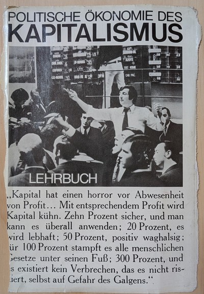 Eine herausgerissene Seite aus einem Lehrbuch, Überschrift "Politische Ökonomie des Kapitalismus".
Unter der Überschrift ein Bild aus einem Börsensaal, mit Händlern in Anzügen, die hektisch gestikulieren und rufen.
Darunter der Text: "Kapital hat einen horror vor Abwesenheit von Profit... Mit entsprechendem Profit wird Kapital kühn. Zehn Prozent sicher, und man kann es überall anwenden; 20 Prozent, es wird lebhaft; 50 Prozent, postiv waghalsig; für 100 Prozent stampft es alle menschlichen Geset…