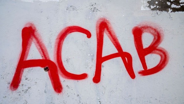 Red graffiti letters "ACAB" spray-painted on a rough, grey concrete wall.