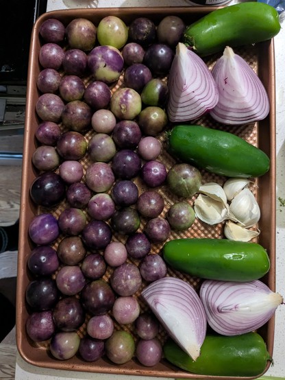 Baking sheet with husked purple tomatillos, red onion, jalepeños, and garlic