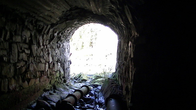 from inside a dried up underground stream tunnel looking out. there is terracotta piping on the ground leading out too.