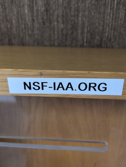 White label with black text "NSF-IAA.ORG" on a wooden surface, conveying an organized and professional tone, with a textured backdrop.