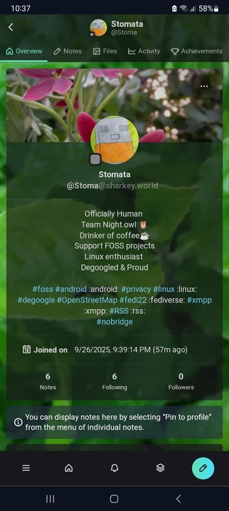 The image is a screenshot of a social media profile page. The profile is for a user named "Stomata" with the handle "[@]Stoma[@]sharkey.world." The profile picture is a cartoonish image of a robot-like character with a green background. The user has a green background with a blurred image of pink flowers and green leaves. The profile includes several attributes: "Officially Human," "Team Night owl," "Drinker of coffee," "Support FOSS projects," "Linux enthusiast," and "Degoogle & Proud." The us…
