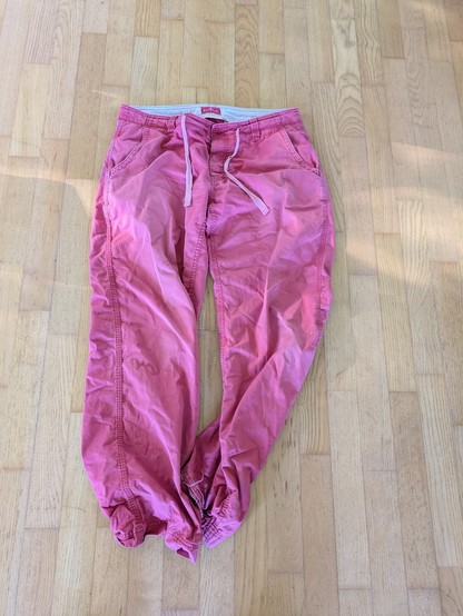Foto einer roten Leinenhose mit Bändeln im Hosenbund. Die Hose liegt auf einem hellen Laminatboden.