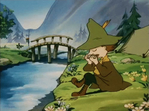 Animated GIF of Snufkin from the 90s Moomin series sitting peacefully on the grass near the wooden bridge, playing his harmonica. His relaxed posture and serene expression reflect his calm connection with nature and music.