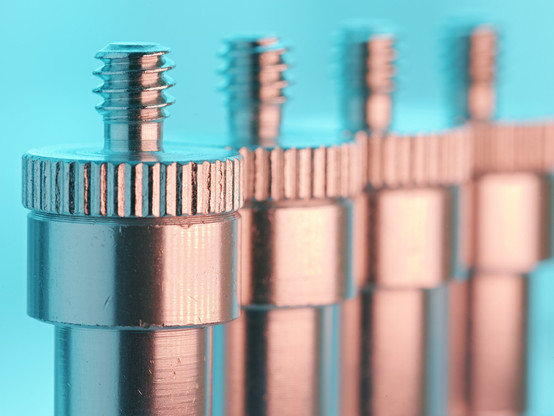 Detailaufnahme von 4 Metall-Bolzen mit Schraubengewinde, von links beleuchtet mit hellem blau, von rechts beleuchtet mit warmen orange.