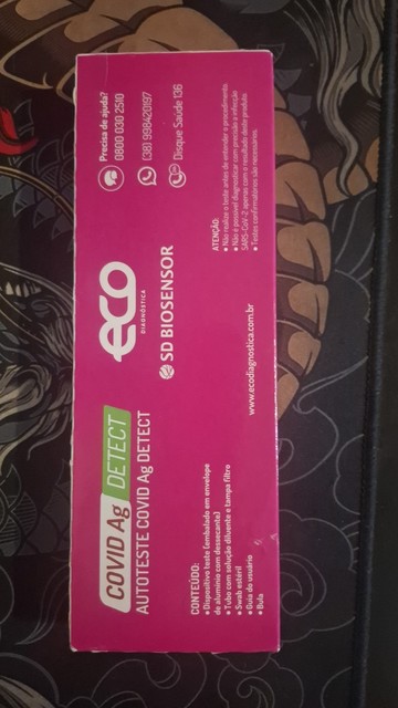 Uma embalagem retangular vertical de um teste rápido COVID-19. A embalagem tem um fundo azul com um padrão geométrico branco. Na parte superior, há o texto "COVID Ag DETECT" em letras brancas grandes. Abaixo, há um logotipo azul com a palavra "ecodiagnostica".

Na parte inferior da embalagem, há a lista de conteúdo:
"CONTEÚDO:
• Dispositivo teste (embalado em envelope de alumínio com dessecante)
• Tubo com solução diluente de tampão filtro
• Seringa estéril
• Solução de lavagem
• Boca de sorvet…