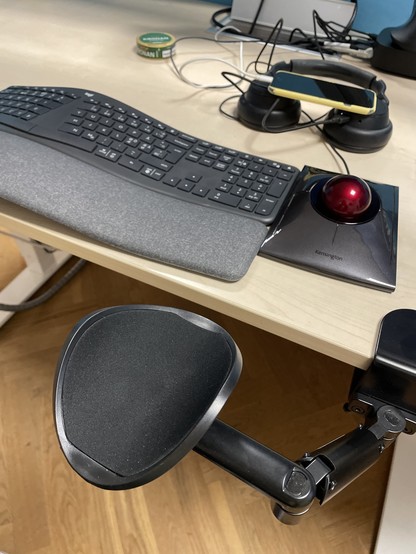 An office desk setup featuring a curved keyboard, a trackball mouse, a pair of  noise cancelling headphones