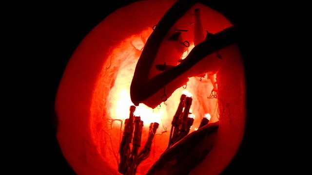 through the gaping hole of an illuminated pumpkin. just a big round hole with a triangle shape at the top right with small shards of pumpkin skewered to it.