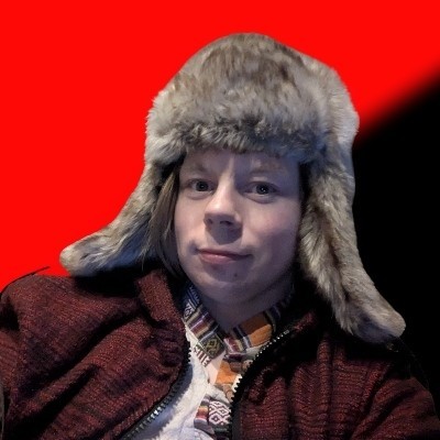 A person wearing a furry hat and a patterned short set against a bold red and black anarchist flag.