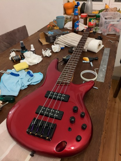 Auf dem Küchentisch liegt ein Vierseitiger E-Bass (Ibanez SR300EB) in candy apple red, drum herum sind Reinigungsutensilien verteilt