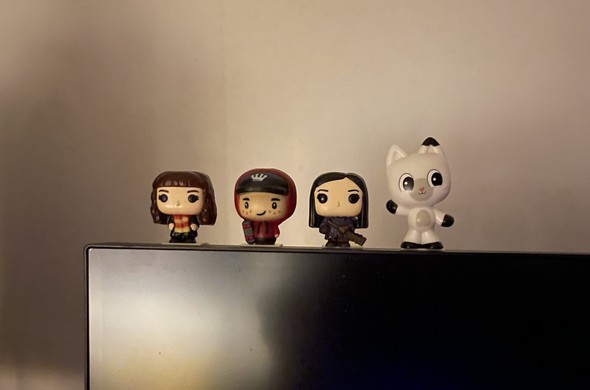 A row of four collectible figurines sits on the edge of a screen. They include a girl with brown hair in a colorful outfit, a boy in a red and black hoodie, a girl in a dark outfit holding a weapon, and a cute white bunny
