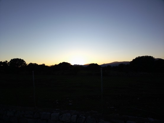 Puesta de sol. se ve el perfil de las montañas oscuras bajo un cielo azul y el brillo del sol ya puesto en el horizonte