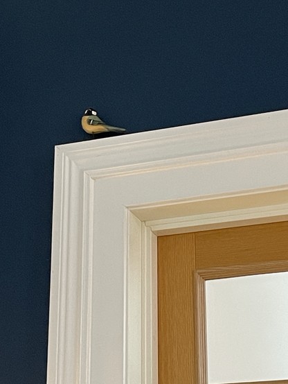 A decorative bird figurine sits on top of a door frame against a dark blue wall. The door is wooden with a paneled design.