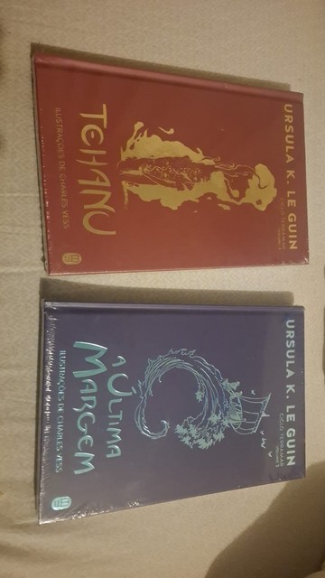 Dois livros estão lado a lado. O livro da esquerda tem uma capa vermelha escura com uma ilustração dourada de um animal de quatro patas que se assemelha a um leão. O texto dourado na capa diz “TEHANU”. Na parte inferior da capa está "ilustrações de charles vess", e no canto superior direito "URSULA K. LE GUIN".

O livro da direita tem uma capa azul escura com uma ilustração prateada de uma criatura serpentina enrolada em torno de uma estrutura semelhante a um navio. O texto prateado na capa diz…
