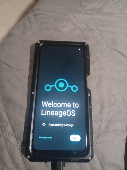 a phone sitting on a gray couch cushion with the Lineage OS welcome screen on the display 