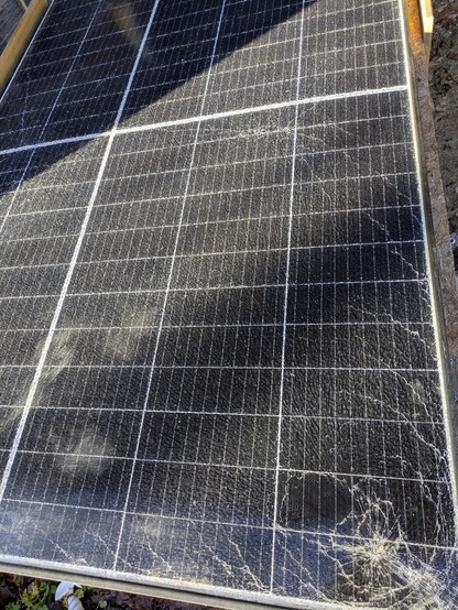 a large solar panel with an obvious impact point and shattered tempered glass across the entire surface