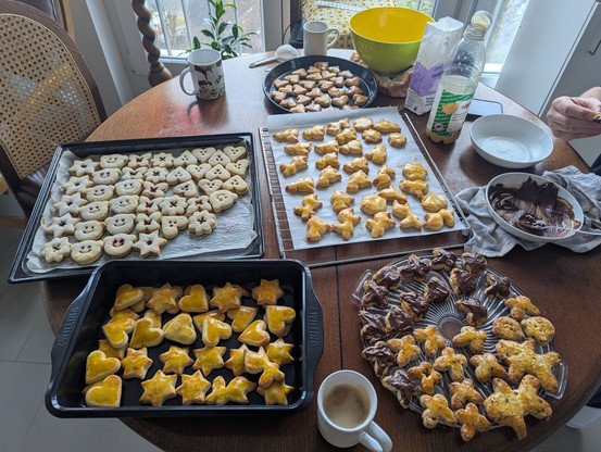 Fünf Bleche und Gitter mit Weihnachtsgebäck auf eine dunkelbraunen Tisch.