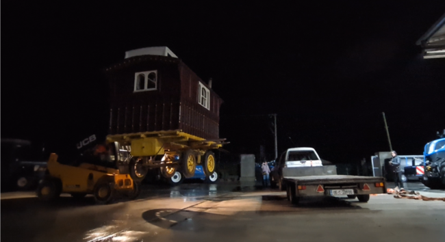 A 19.c wooden showman's wagon (with slightly-more-modern wheels) being loaded onto a trailer with a compact telehandler