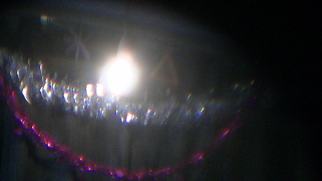 xmas tinsel and stuff on our curtains behind the electric light. it looks like a smiley face. it is a bit blurry