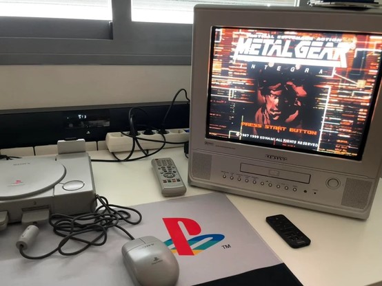 A TV on a desk next to a playstation console running metal gear solid.
