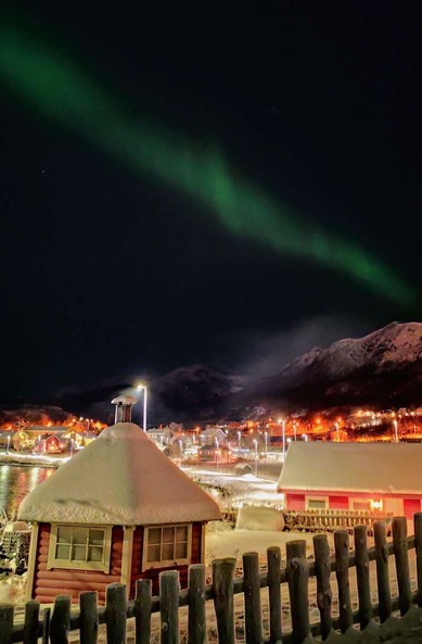 Picture of the Aurora Borealis over a snow covered village, with mountains in the background