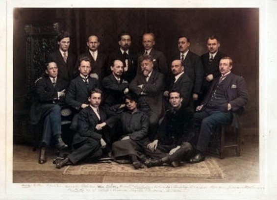 A vintage photograph showing thirteen men in formal attire, posing together in a structured arrangement.