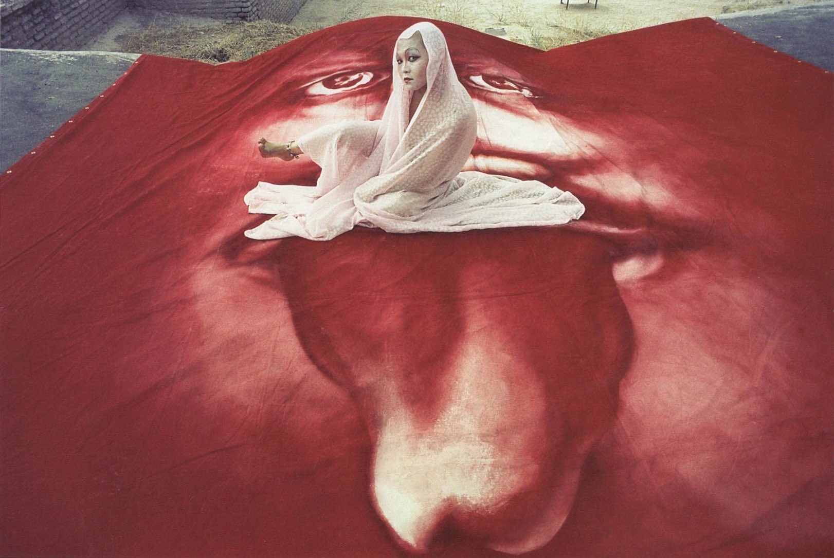 this woman sits on a large red distorted face with its tongue out