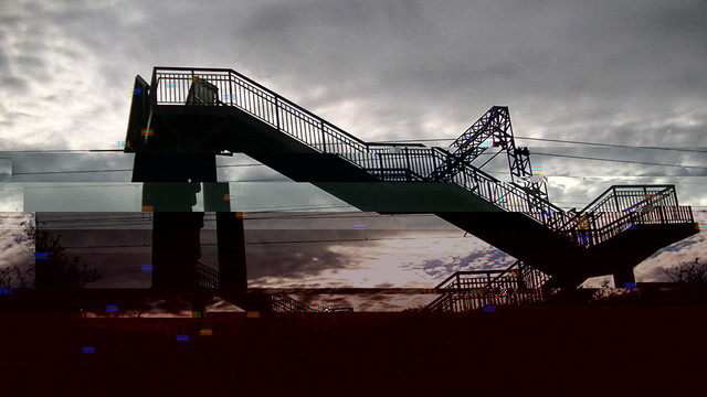 a glitched image of a steel railway footbridge