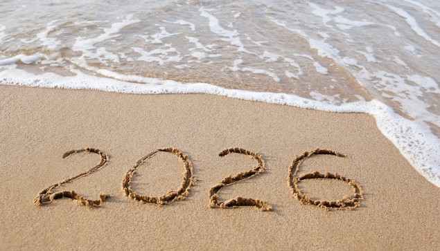 "2026 is written in the sand on a beach, with gentle ocean waves approaching. The scene conveys a sense of time, transition, and natural beauty."