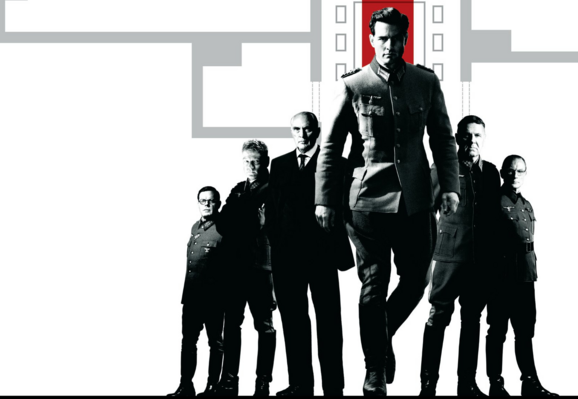 A part of the poster for the films Valkyrie (2008).

The image is of a group of men in lined up on either side of Tom Cruise. The line is actually in a arrow-shape. Since Tom Cruise is in the front he is bigger than the others but he isn't just a little bigger, he looks like the tallest man in the world.