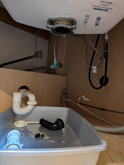 View inside cabinet under sink where garbage disposal was. Showing p trap drain, water lines and dishwasher hose.