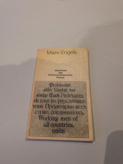 Front cover of a small beige paperback titled “Marx/Engels – Manifest der Kommunistischen Partei,” featuring the slogan “Working men of all countries, unite” printed in multiple languages inside a bordered panel.