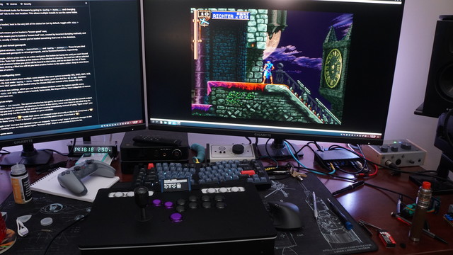 BizHawk running on the right-hand monitor with a fight stick on top of the desk.