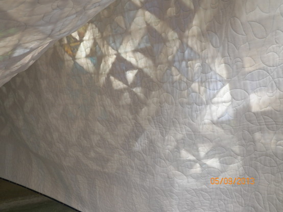 Eine Bettdecke (ein Patchwork-Quilt) hängt über eine Wäschleine, der Fotograf ist unter die Decke geschlüpft und hat ein Foto von der Rückseite aufgenommen. Das Muster der Oberseite scheint durch.