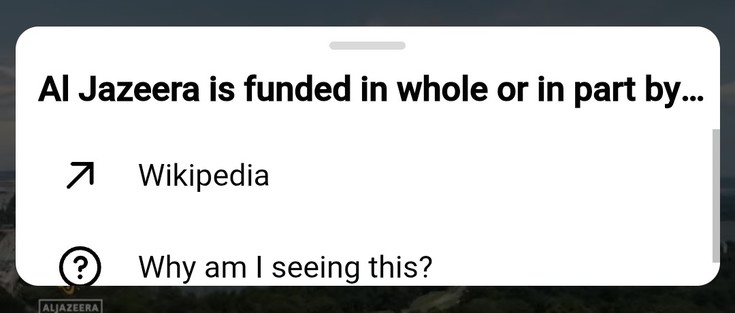 A popup on a YouTube video, on mobile, which says, on the first line, "Al Jazeera is funded in whole of in part by...", and on the second, an arrow icon next to the word "Wikipedia". On the third line, a circled question mark next to the text "Why am I seeing this?"