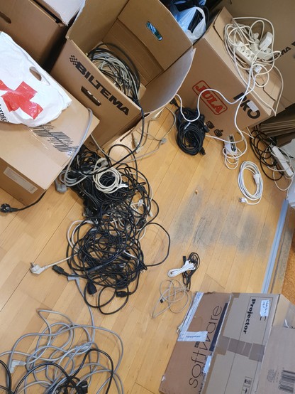 Boxes filled with power cables, cables lying on the floor sorted into several heaps.