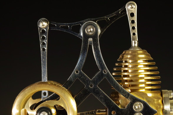 Metallteile, die silbrig und golden glänzen. Es ist eine Detailaufnahme von einem Stirlingmotor. 